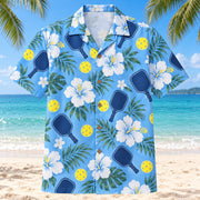 Front view of Blue Hibiscus Rally Pickleball Hawaiian Shirt with original white hibiscus flowers, navy pickleball paddles and bright perforated yellow balls on an airy blue ground